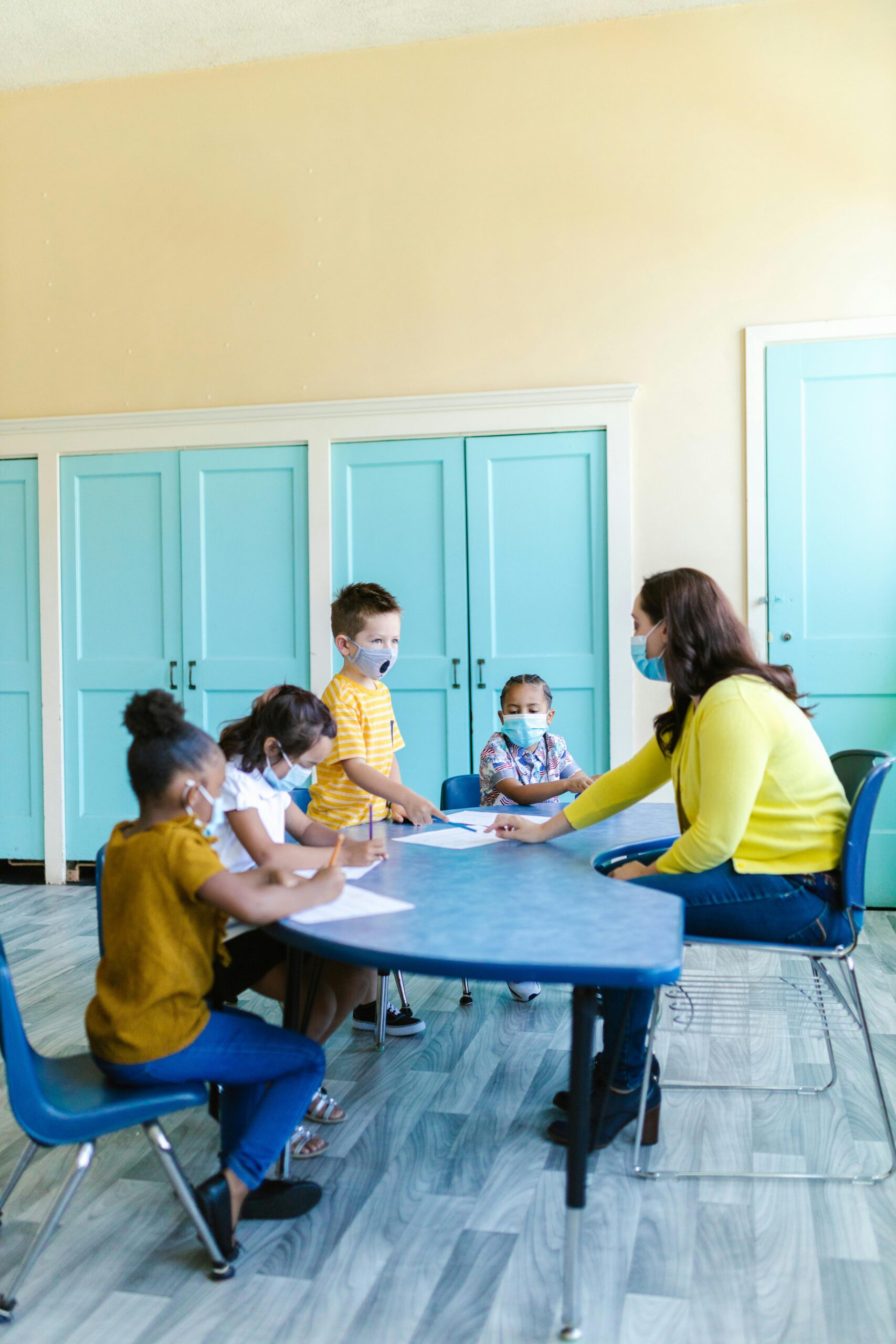 Children learning with a teacher wearing masks in a vibrant classroom.