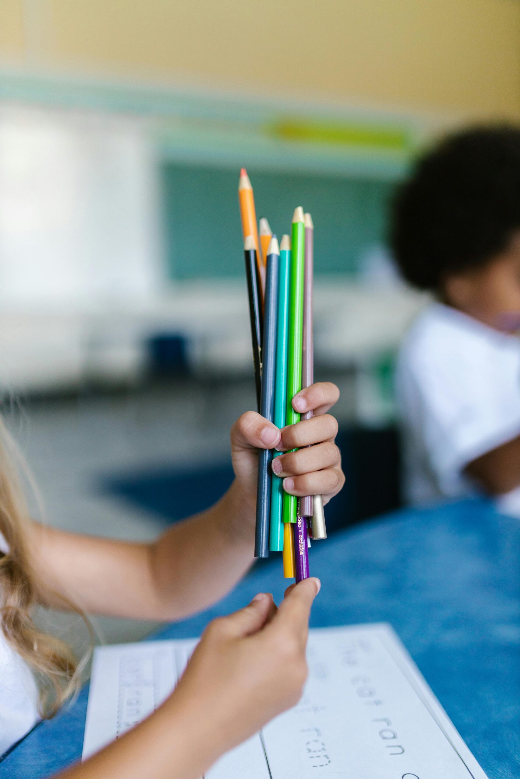 Two children holding a bunch of colorful pencils, indoors in a learning environment.